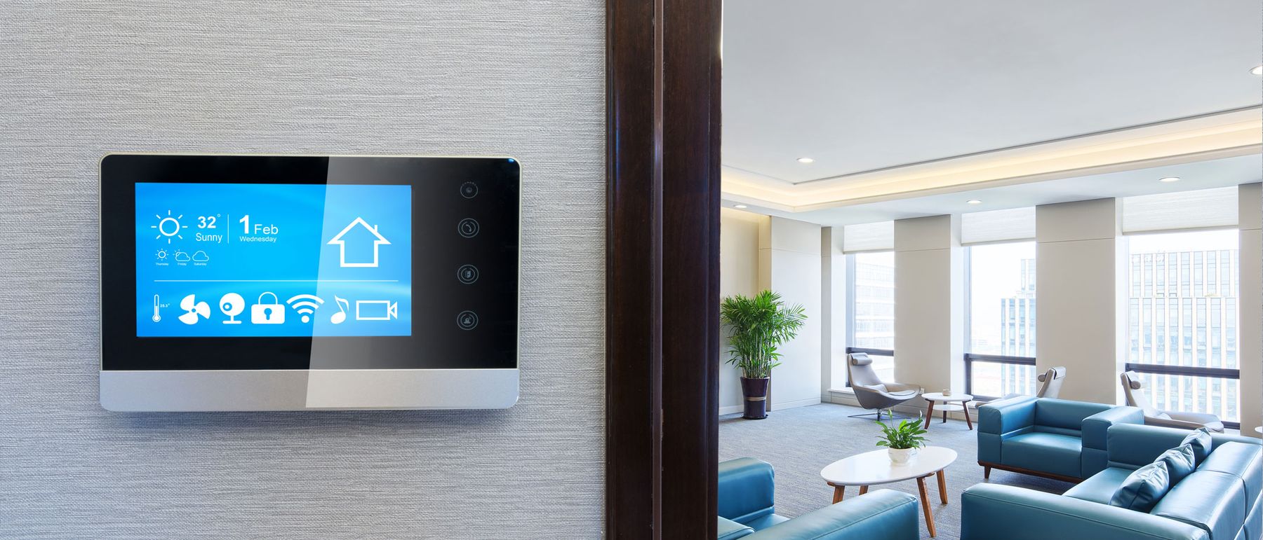 Bediendisplay an der Wand eines hellen Wohnraums mit Sofas und großen Fenstern